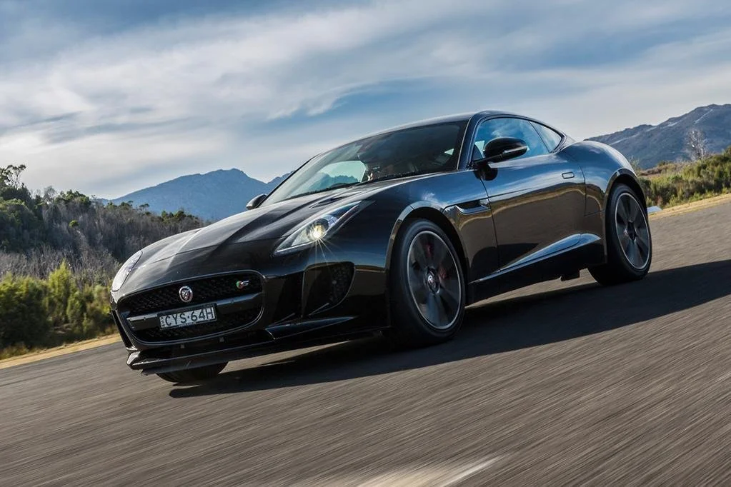 Black Jaguar sports car driving on a road with mountains in the background.