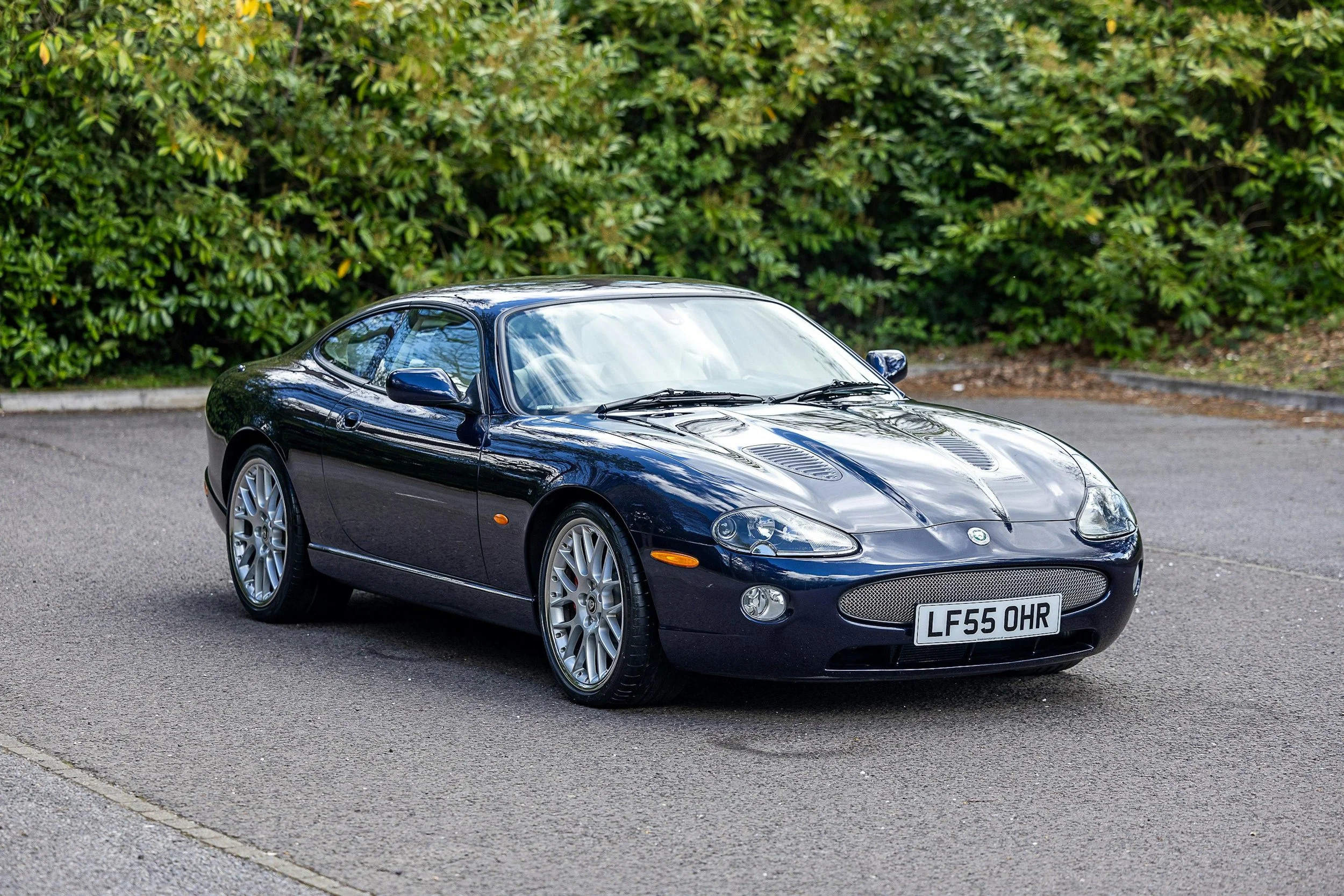 A black sports car with the license plate 'LF55 OHR' parked on a gravel area with greenery in the background.