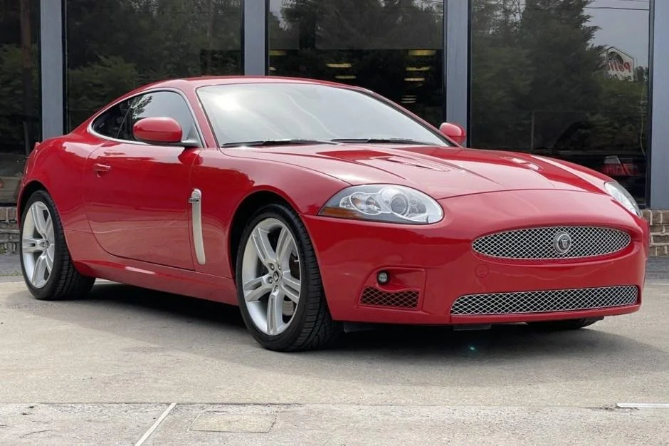 Red two-door coupe car parked outside a building with large glass windows.