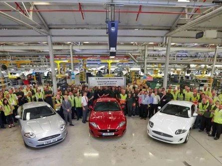 Automobile assembly line with workers in safety vests and three finished cars: a silver, a red, and a white vehicle.