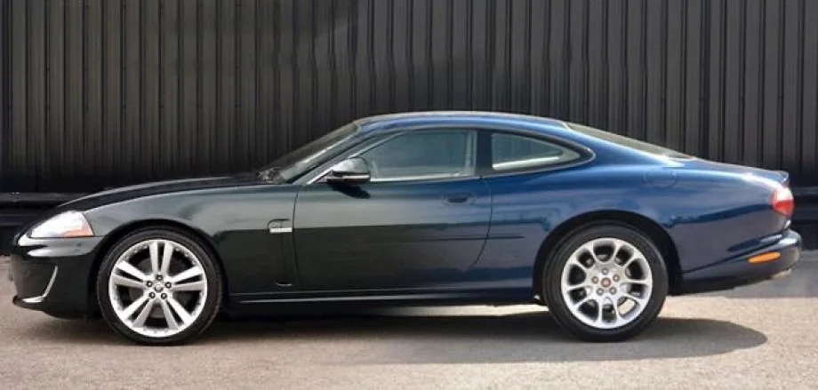 Black and blue two-door coupe sports car parked on pavement in front of a black wooden fence.