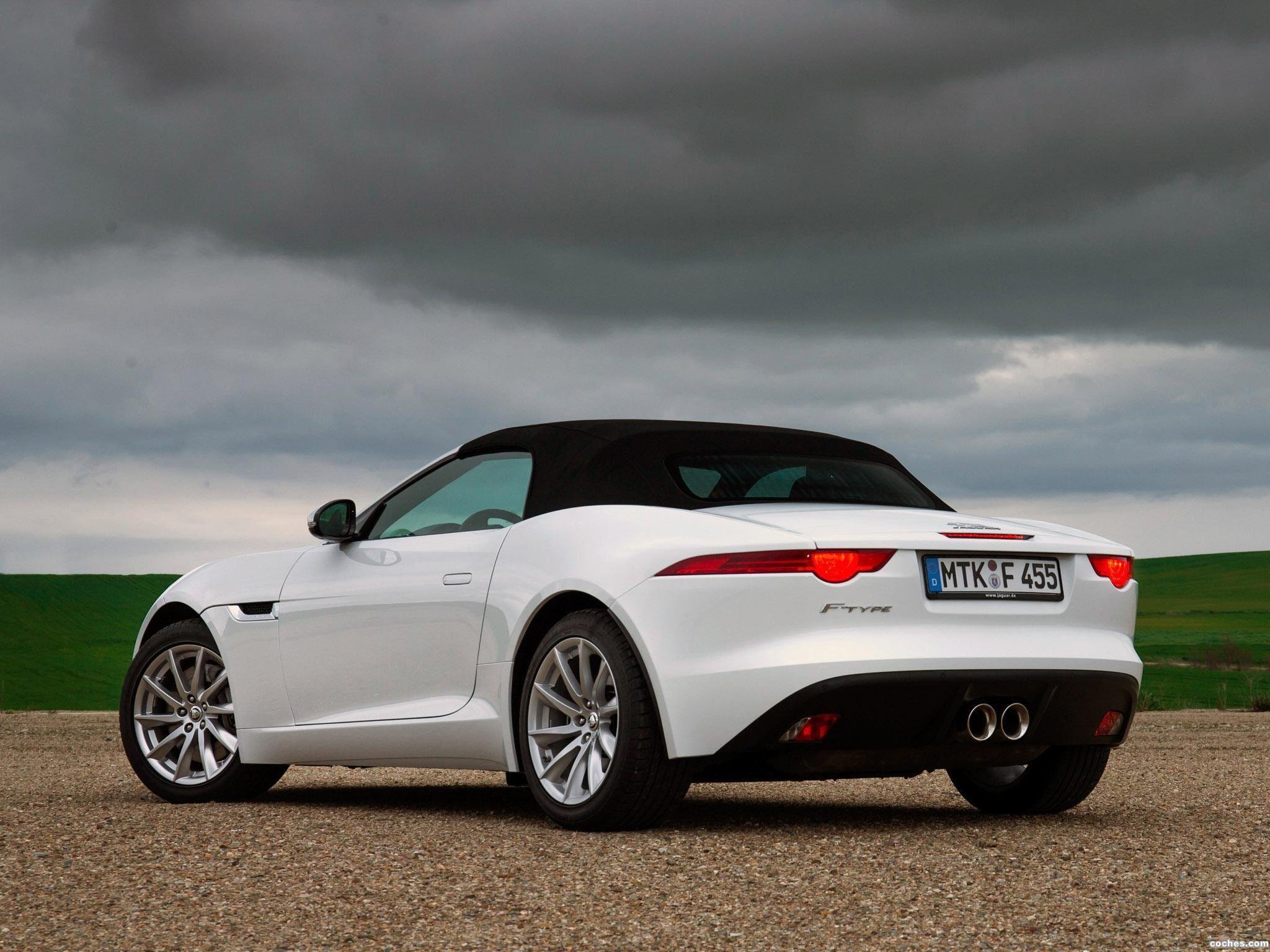 A white sports convertible car parked on a gravel surface backlit by a dark, cloudy sky.
