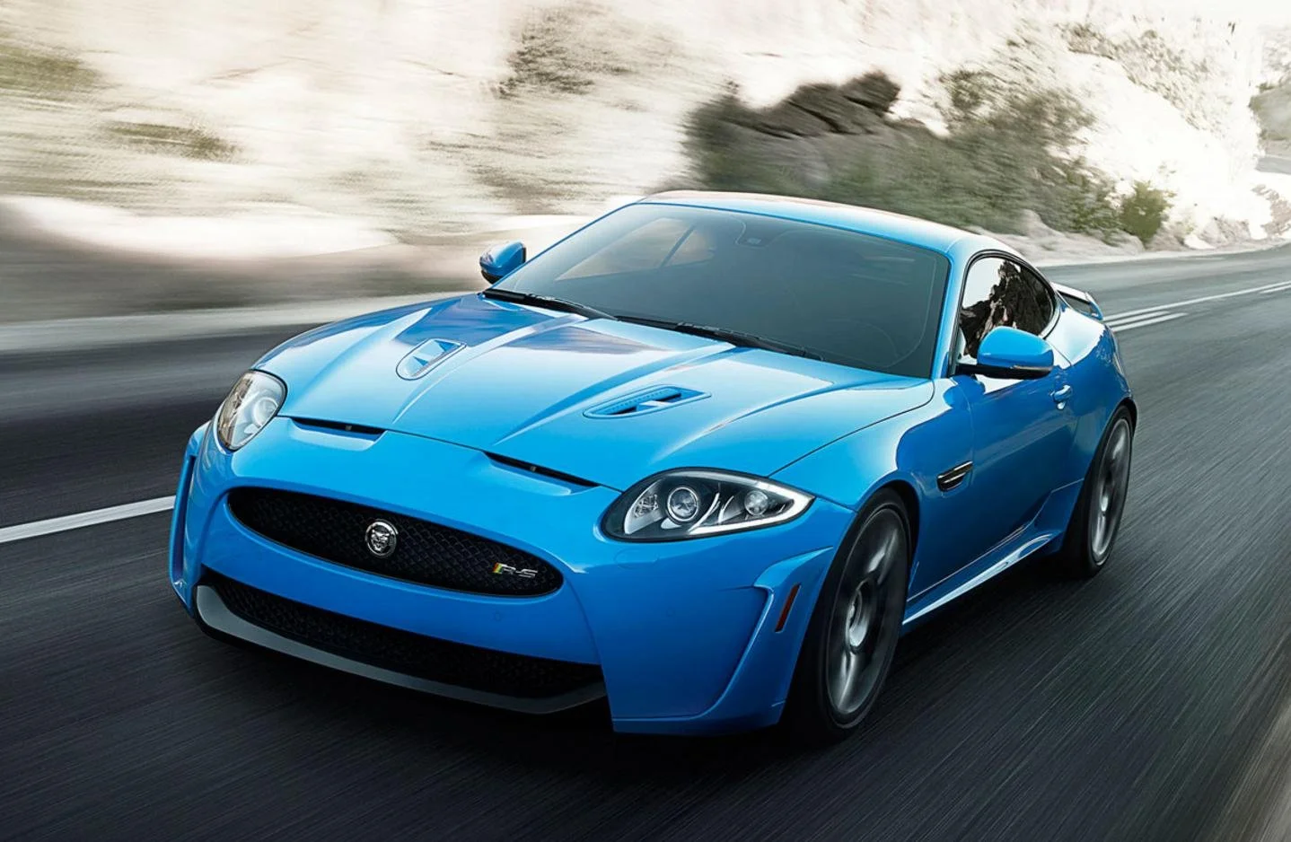A blue sports car driving on a highway with a desert landscape in the background.