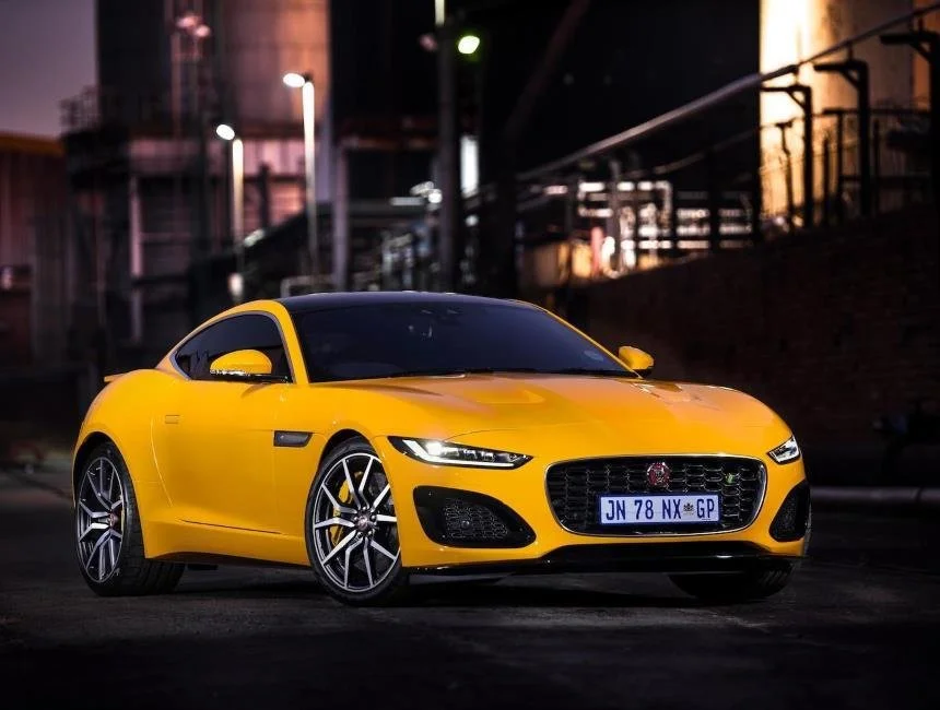 A yellow sports car parked on a city street at night with illuminated buildings and streetlights in the background.