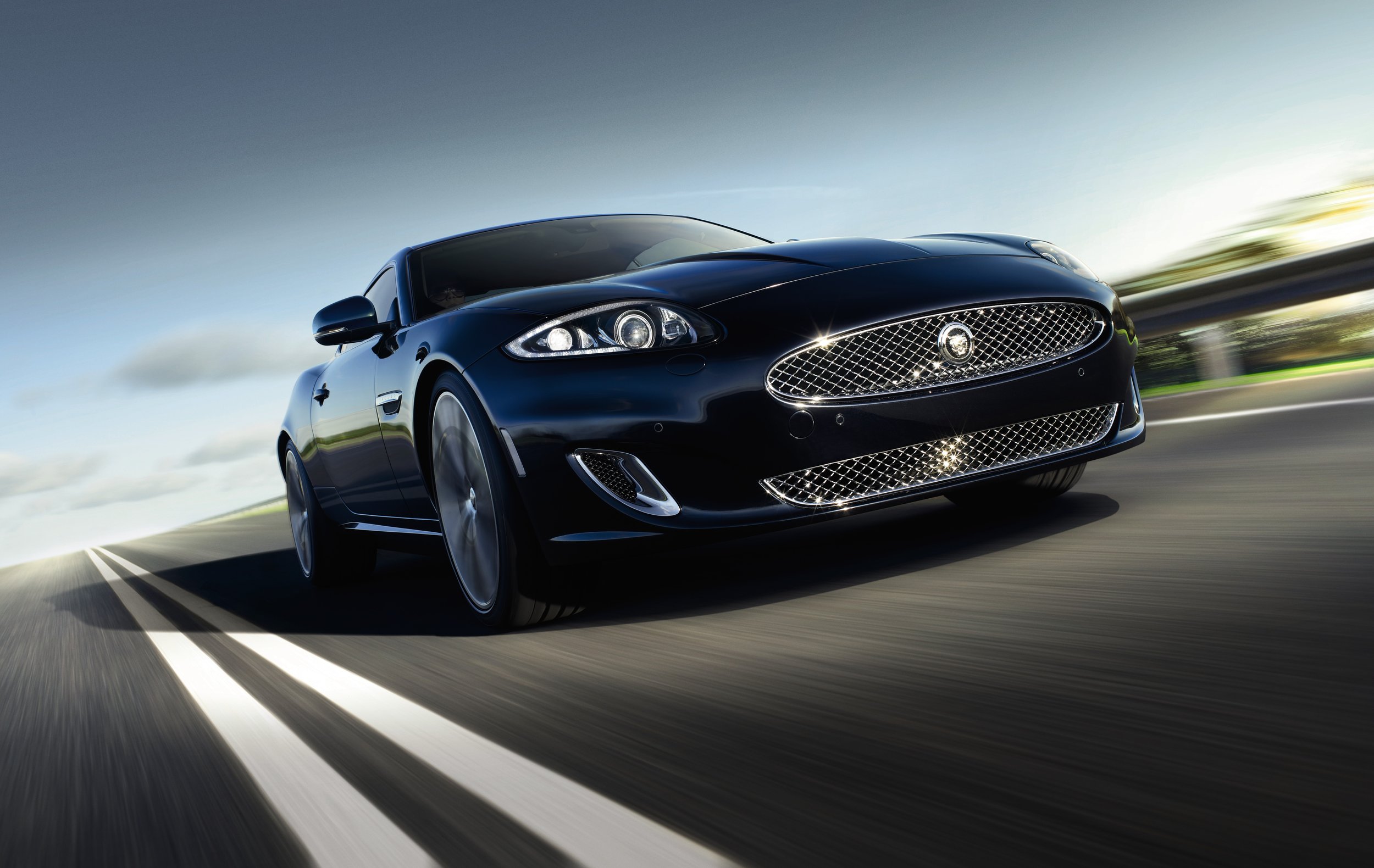 A sleek black sports car speeding down a highway at sunset or sunrise, with motion blur on the road and background.
