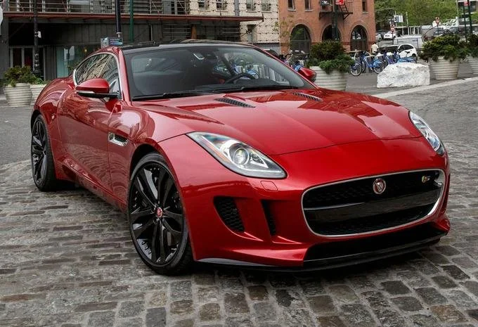 Red sports car parked on cobblestone street with buildings and plants in the background.