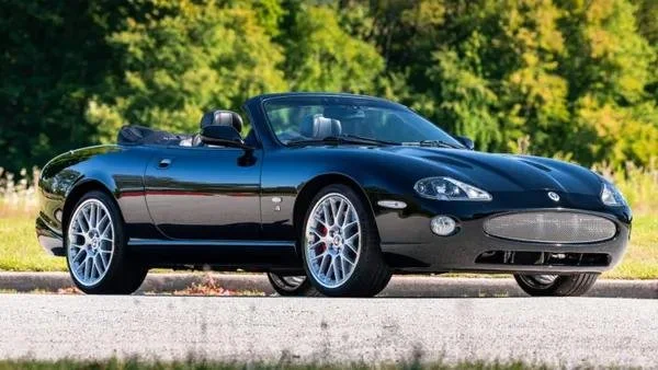 A black convertible sports car parked on a road with a background of green trees and blue sky.