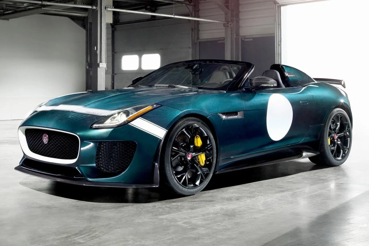 Green sports car with an open top, black wheels, yellow brake calipers, and a white circle on the side, inside a garage.