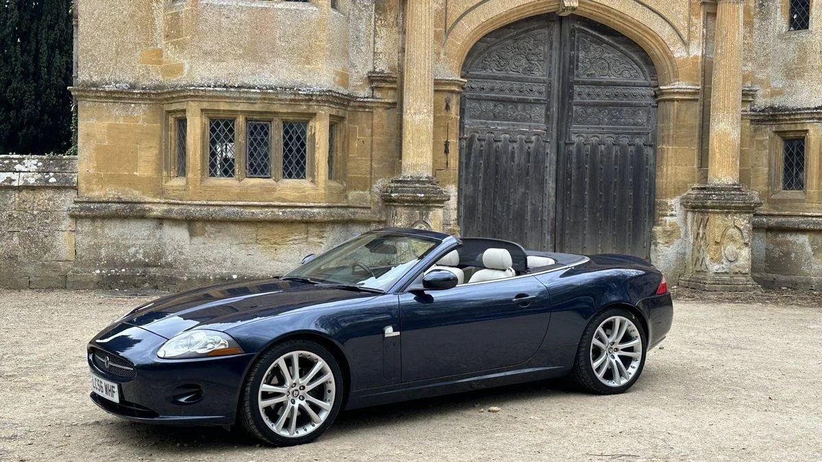 A black convertible Jaguar car parked in front of an old stone building with arched wooden doors and small leaded glass windows.