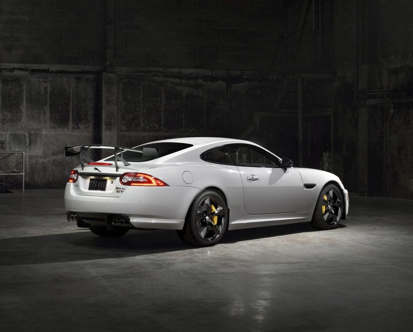 A white sports car with a spoiler and yellow brake calipers parked in an industrial warehouse.
