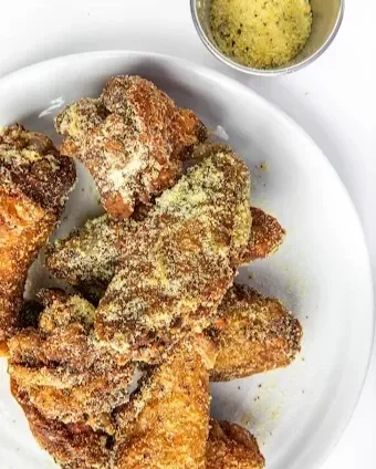 Coated fried chicken wings on a white plate, with a bowl of dipping sauce.
