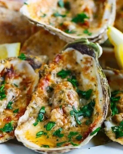 Oysters topped with cheese, herbs, and seasoning, garnished with chopped green onions and lemon wedges.