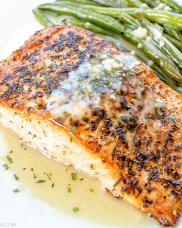 Grilled salmon fillet topped with herb butter, served with green beans.