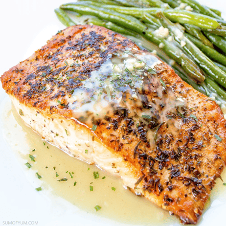 A plate with a cooked salmon fillet topped with herbs and sauce, served with a side of cooked green beans.