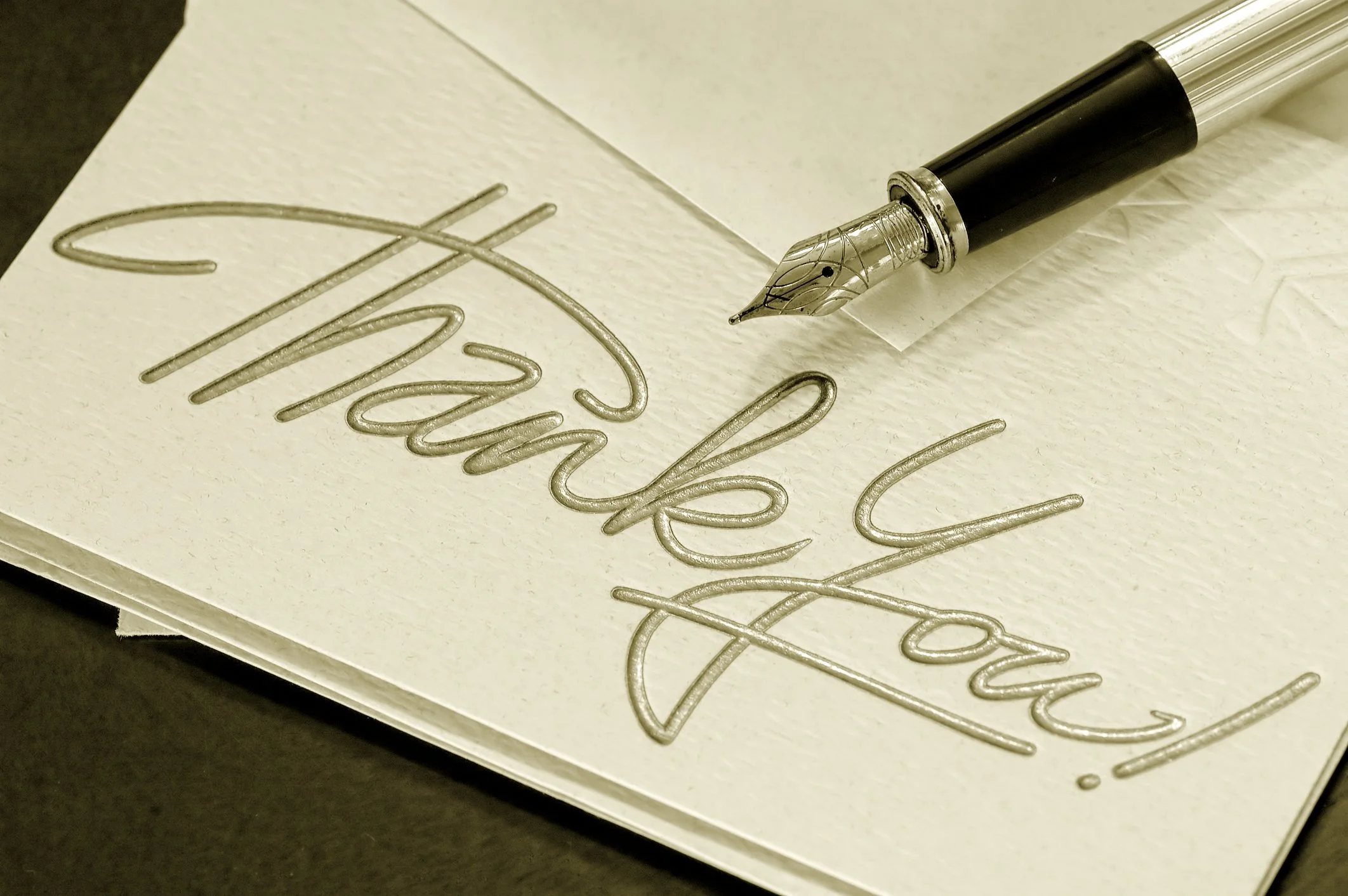 Close-up of a fountain pen writing on textured white paper, creating cursive text that appears to spell 'Thank you.'