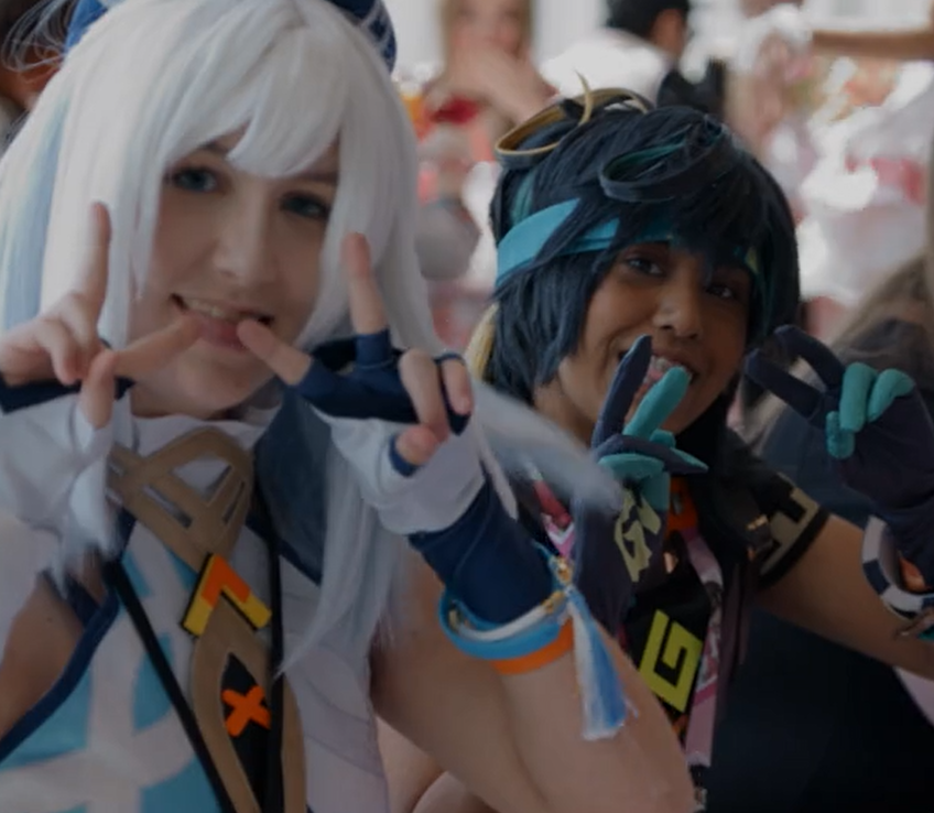 Two people dressed as anime characters at a convention, making peace signs and smiling.