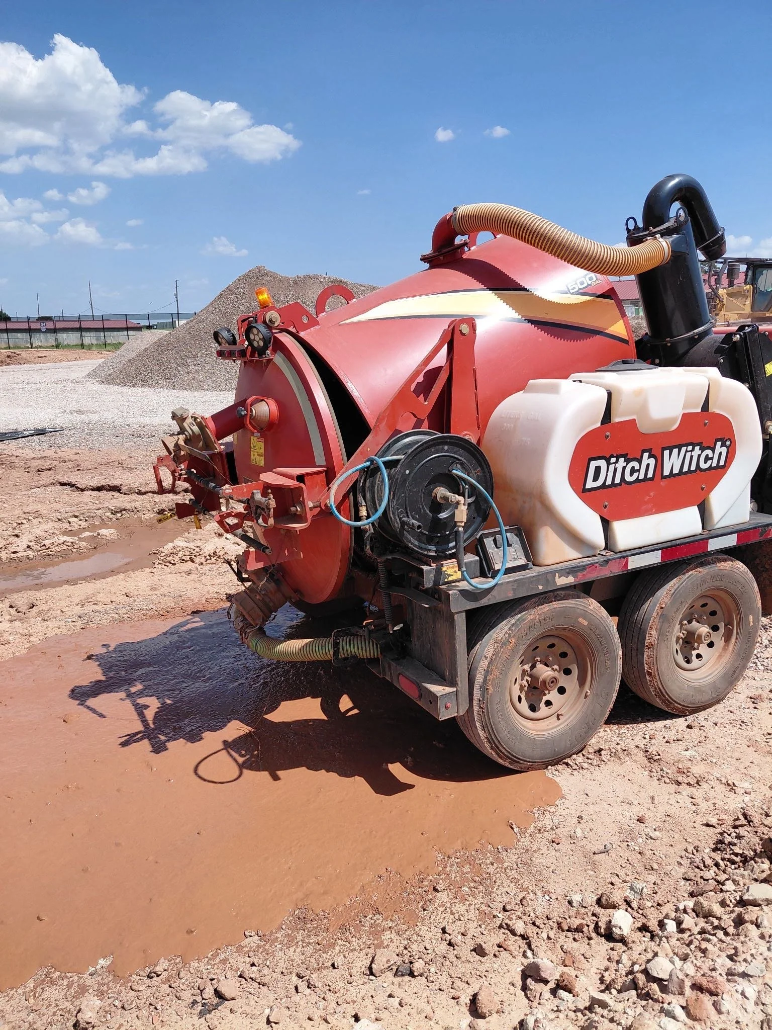 A portable industrial soil or asphalt compactor machine labeled "Ditch Witch" on a construction site with dirt and gravel, under a blue sky with some clouds.