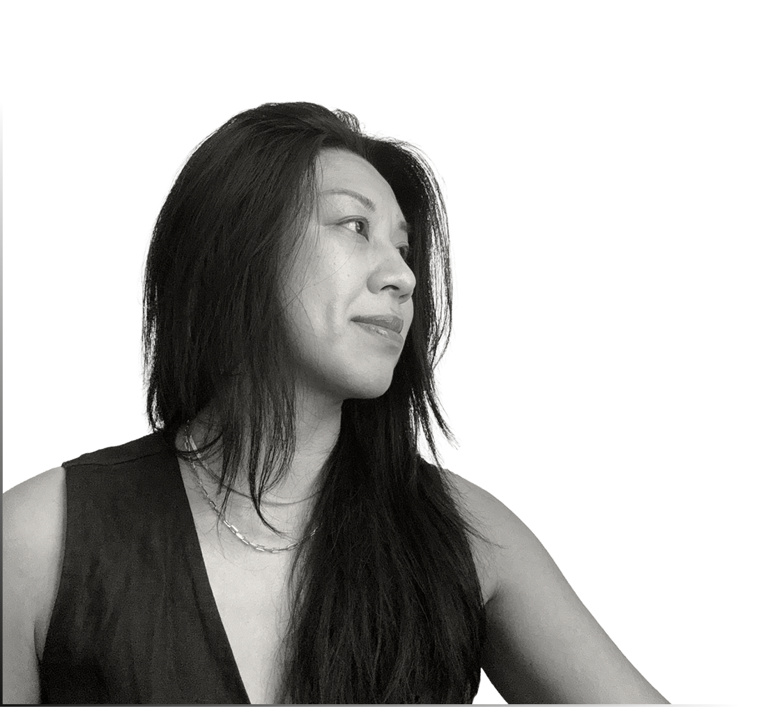 Black and white photo of a smiling woman with long dark hair, wearing a sleeveless top and a necklace, looking to the side.