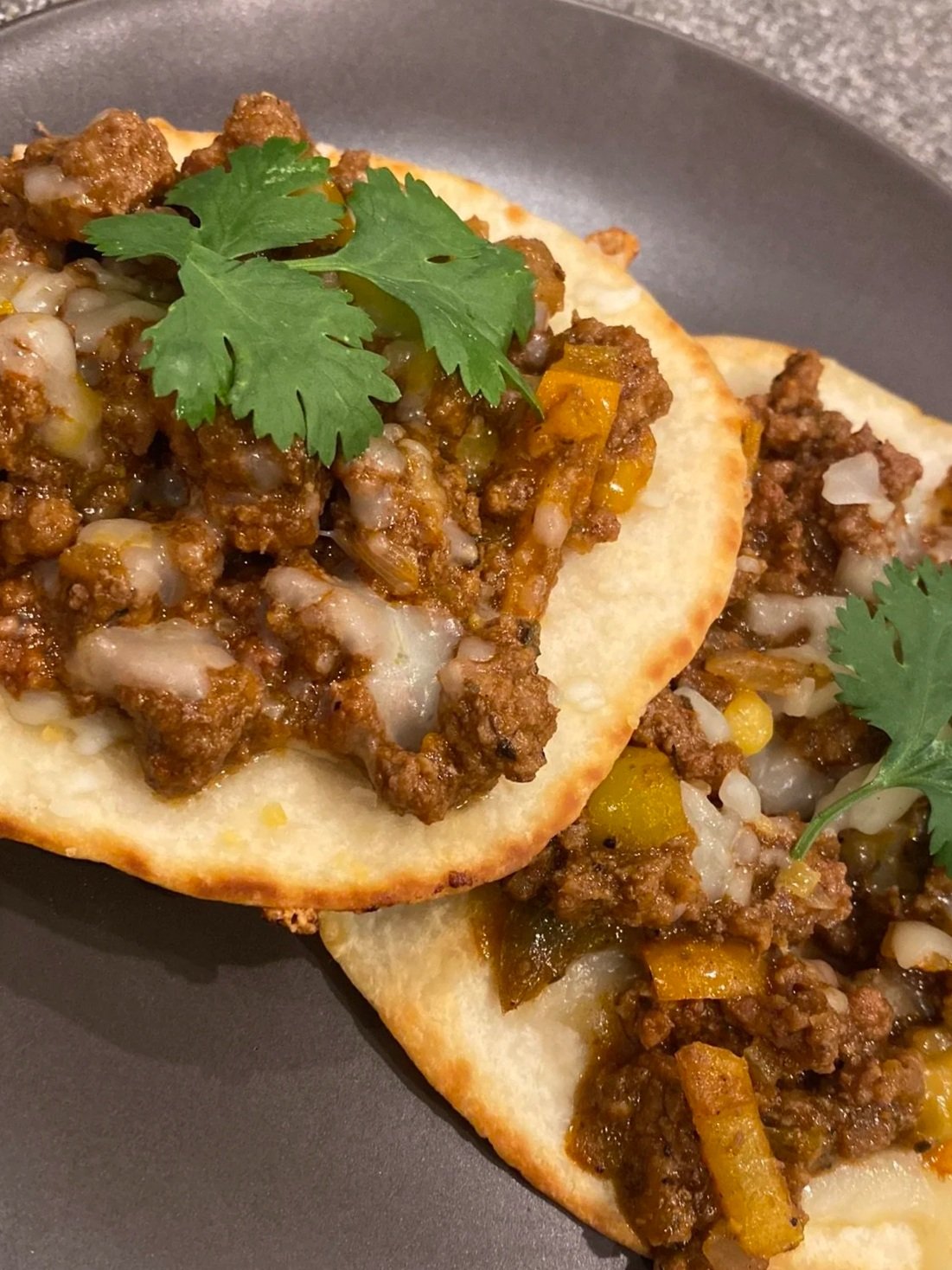 Close-up of two beef tacos topped with cilantro on a black plate.