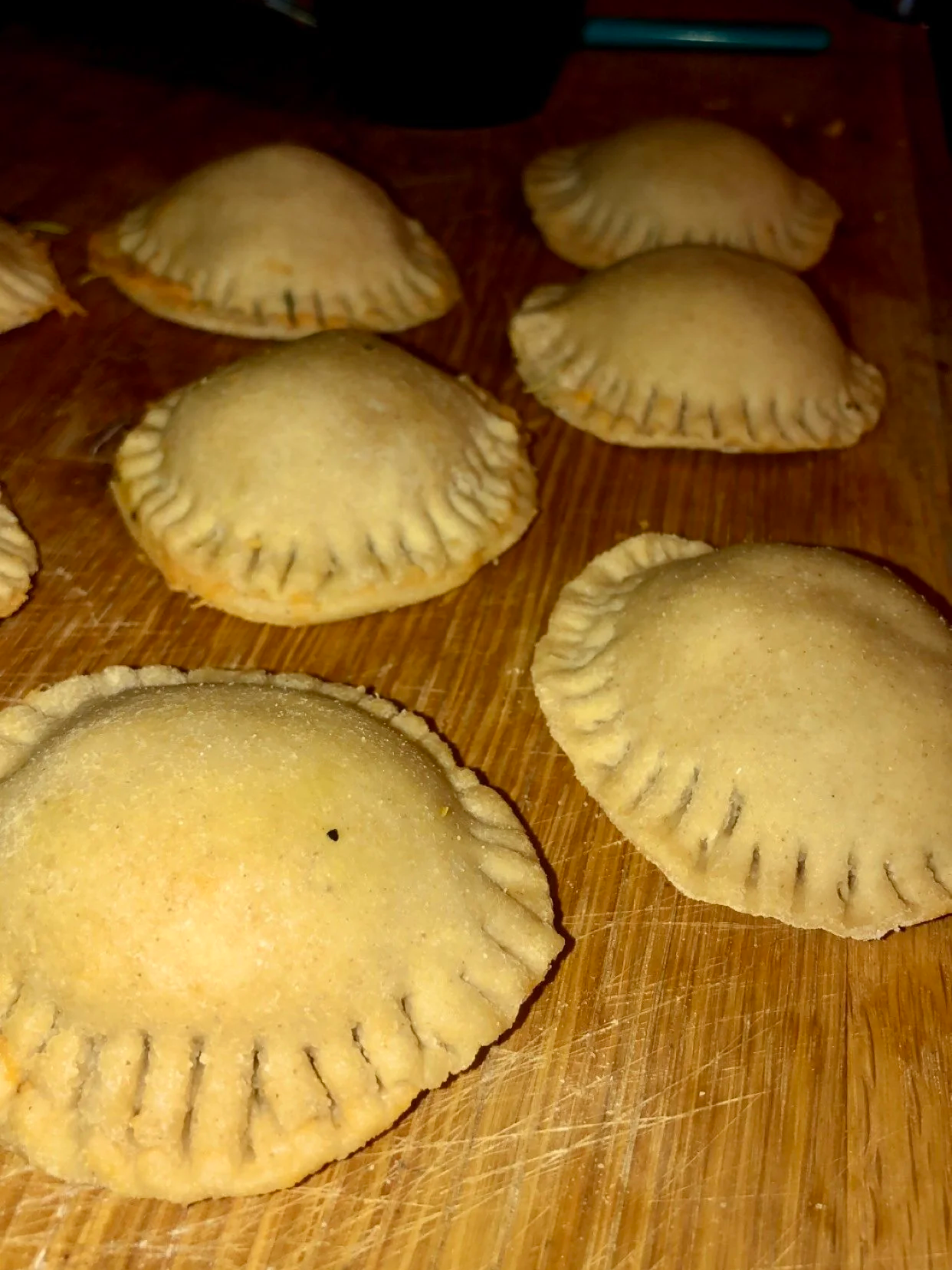 Uncooked handmade raviolis on a wooden cutting board.