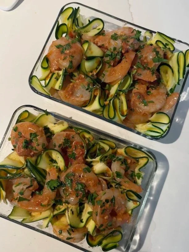 Two glass containers of zucchini noodles topped with cooked shrimp and chopped herbs.