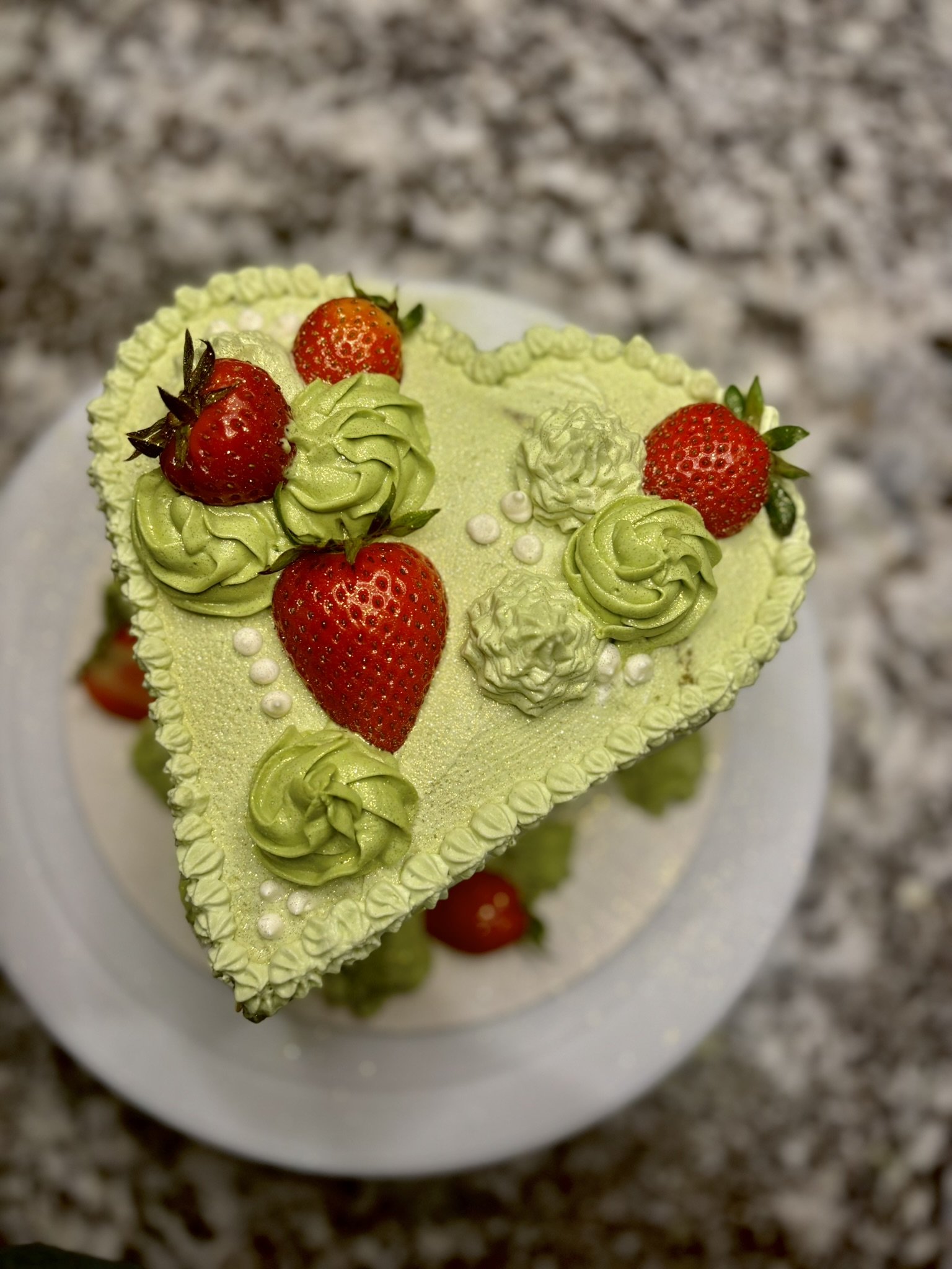 Heart shaped matcha cake with strawberry filling, topped with strawberries and matcha whipped cream, and rosettes.