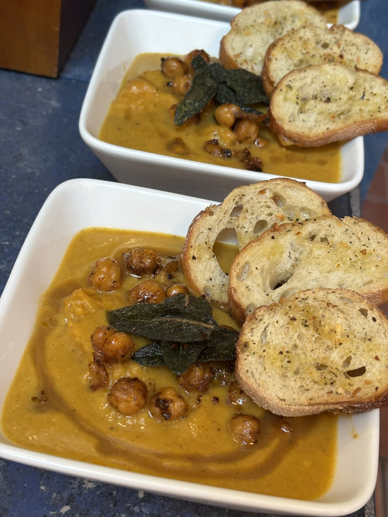 Bowl of butternut squash soup with chickpeas garnished with crispy fried sage and a baguettes.