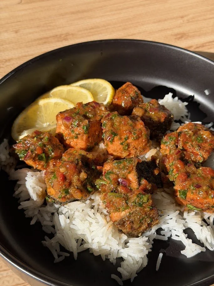 Bowl of cooked white rice topped with spicy salmon coated in a green and red chili sauce, garnished with lemon slices