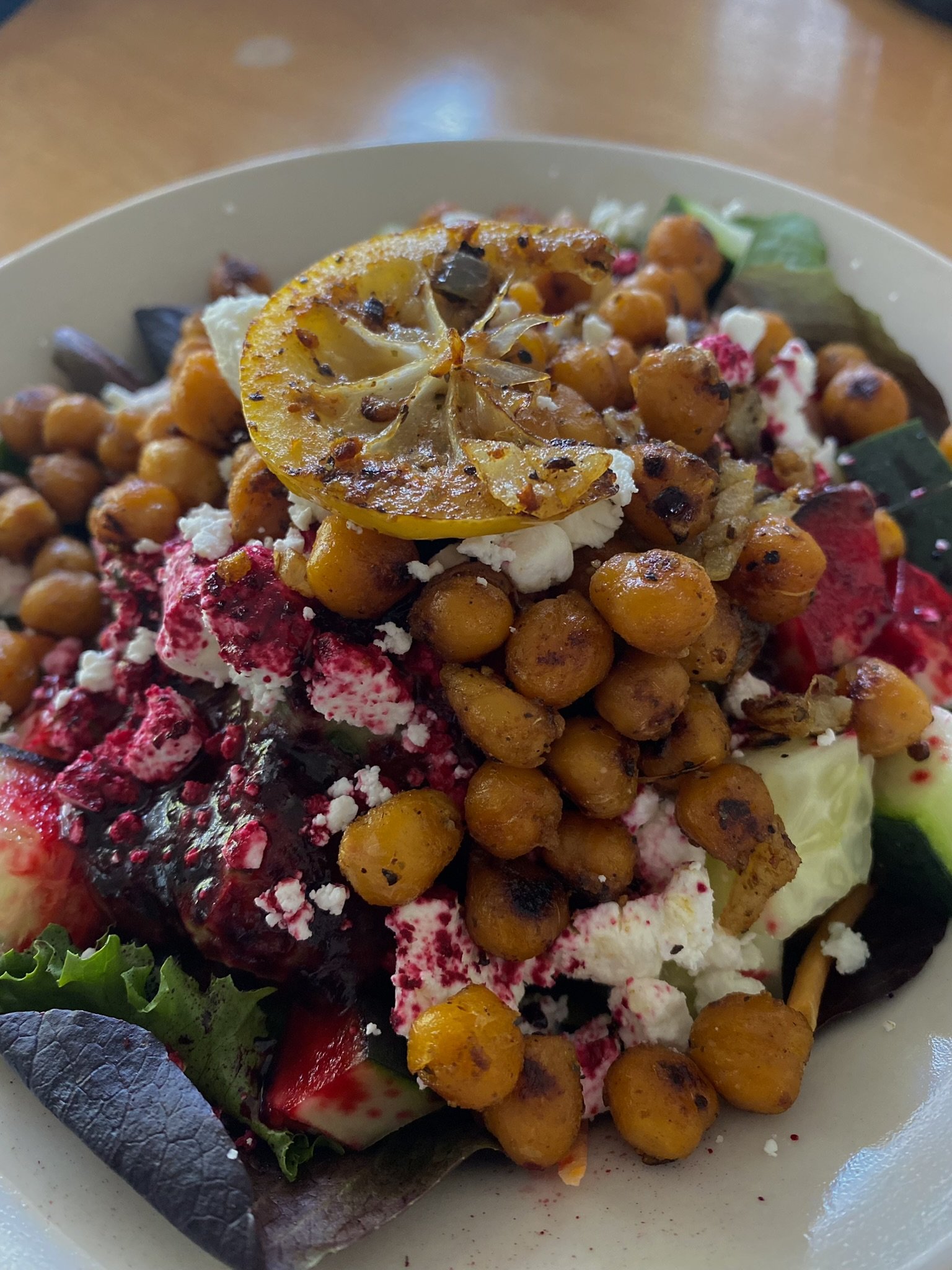 Close-up view of a plate with roasted chickpeas, beet goat cheese, grilled lemon slice, and mixed salad greens.