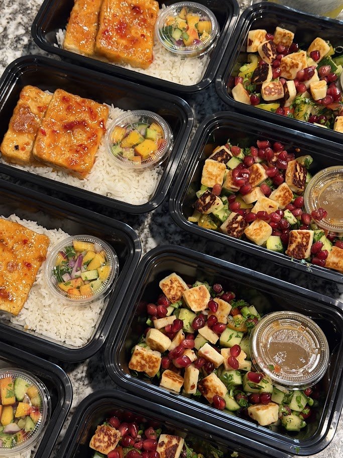 Meal prep containers with baked sweet chili tofu, white rice, and peach cucumber salsa and a mediterranean salad with pomegranate seeds, cucumber, and tomato, and grilled hot honey halloumi served with a tahini - pomegranate molasses dressing.