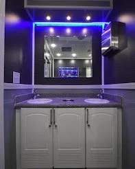 A bathroom vanity with a dark countertop, a white cabinet, and a large mirror framed with blue LED lights.