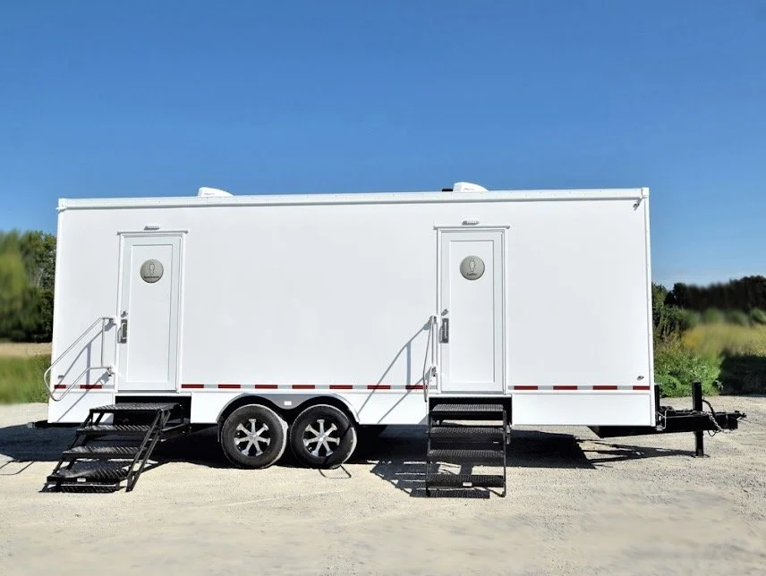White mobile trailer with two doors, stairs, and tires, set on a gravel surface under a blue sky.