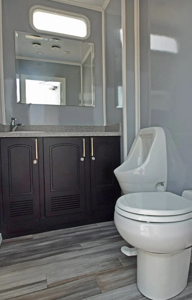 A modern bathroom featuring a black vanity with silver handles, a grey countertop, a large mirror, a small horizontal window above the mirror, and a white toilet with a built-in bidet and a high-backed seat. There is a door reflected in the mirror an