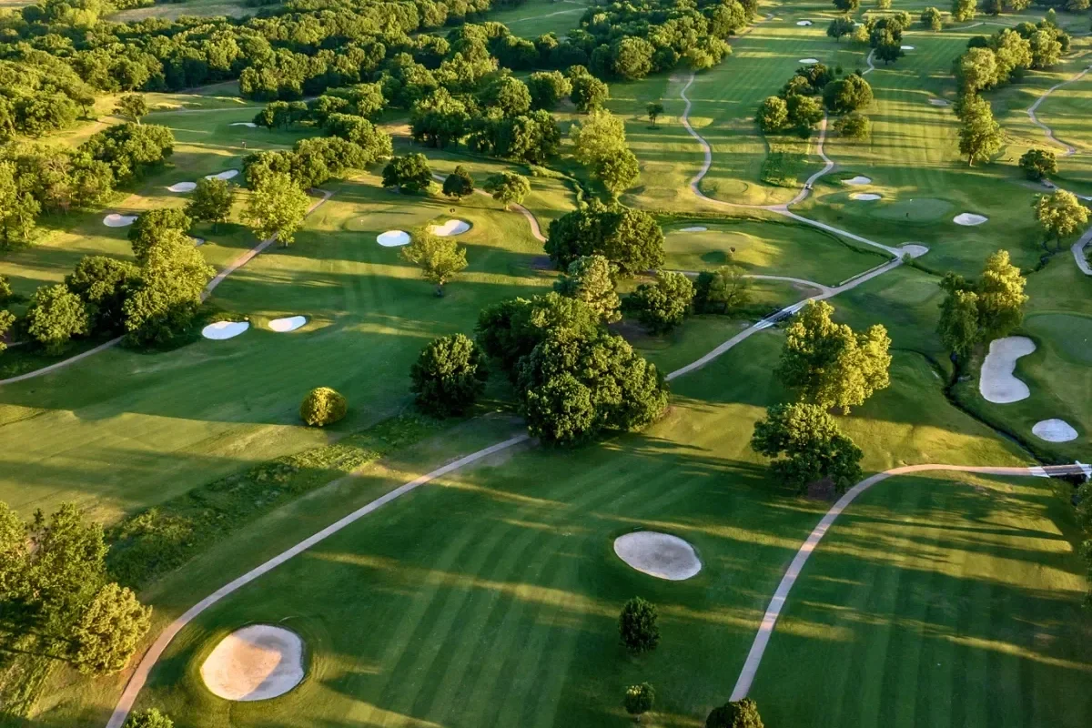 Aerial view of a golf course with green fairways, sand traps, and scattered trees.
