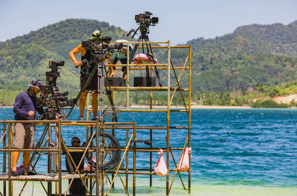 7C team members sitting on wooden poles above turquoise water