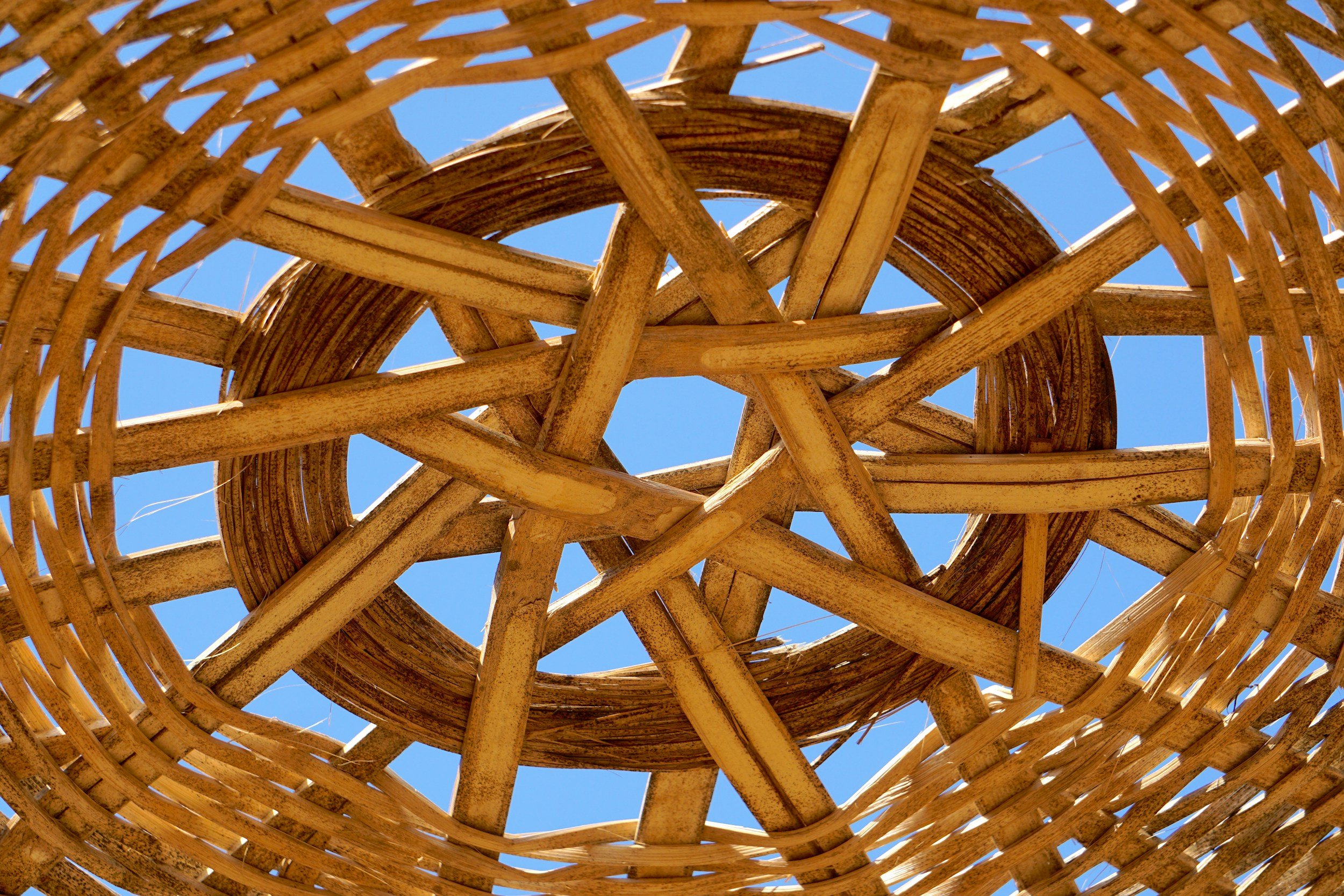 Looking up through a woven wicker basket towards a clear blue sky.