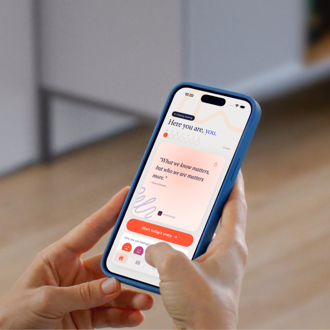 Close-up of a person holding a smartphone with a mental health app open, displaying a quote and an option to start a daily journal entry.