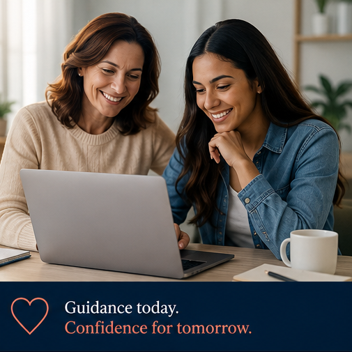 Two women smiling and looking at a laptop screen together at a desk with a coffee mug and notebook, in a bright room.
