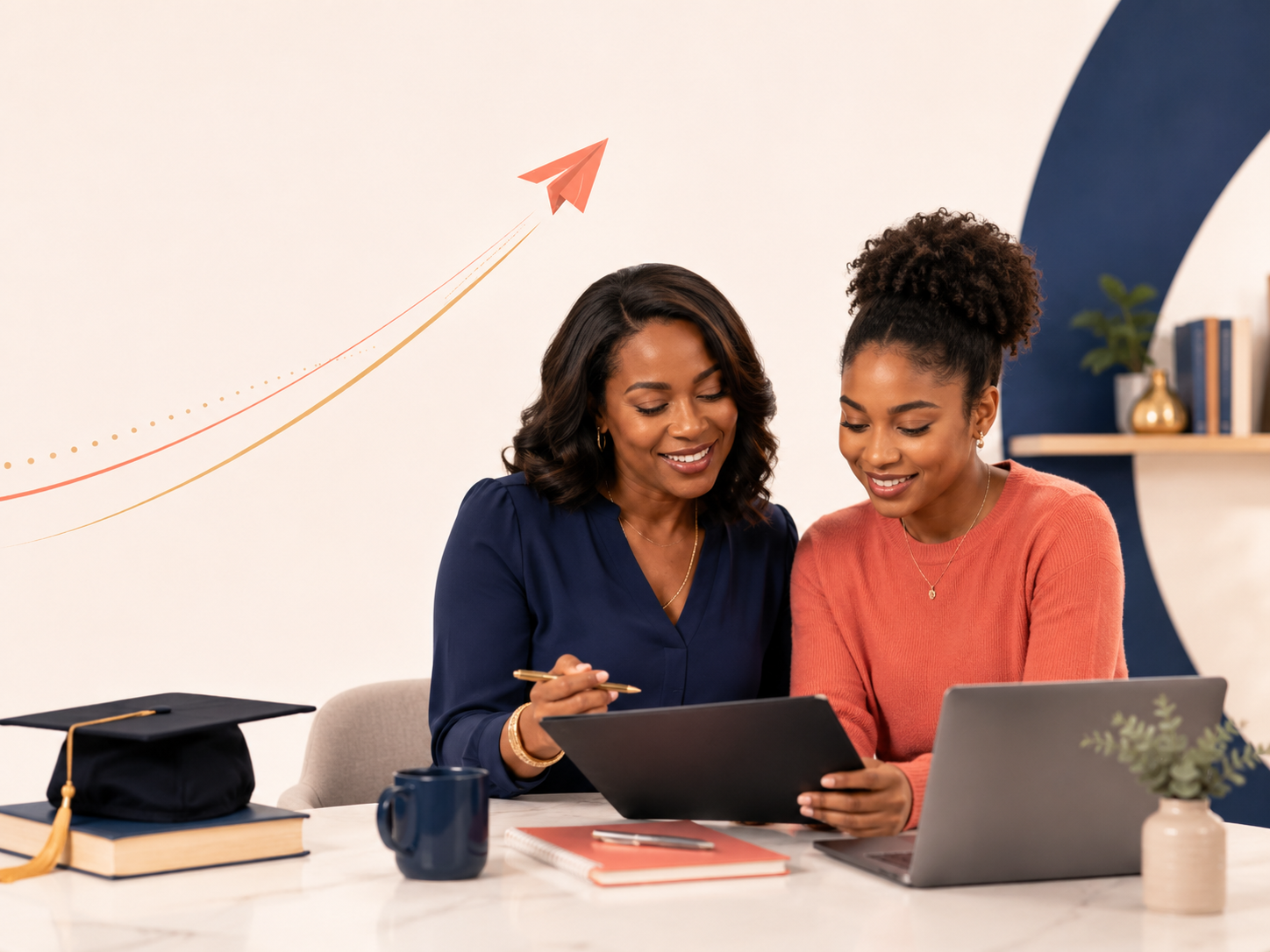Two women sitting at a desk, looking at a tablet together, smiling. Desk has a graduation cap, a book, a mug, a notebook with a pen, and a laptop. Background features a white wall with a blue curved accent and a shelf with plants and books.