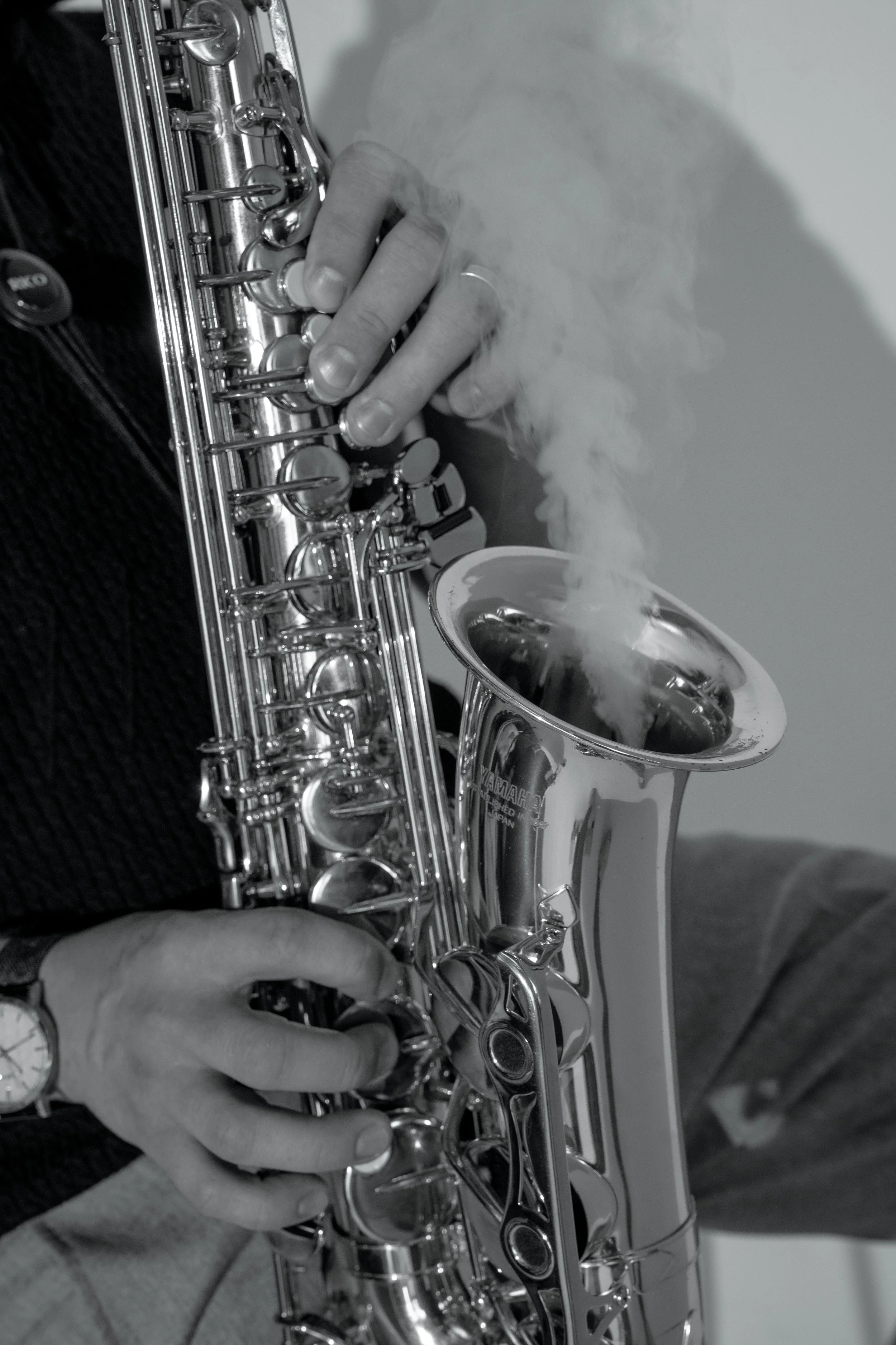 Close-up of a person playing a silver saxophone, focusing on the hand pressing the keys, with smoke coming out of the instrument's bell.