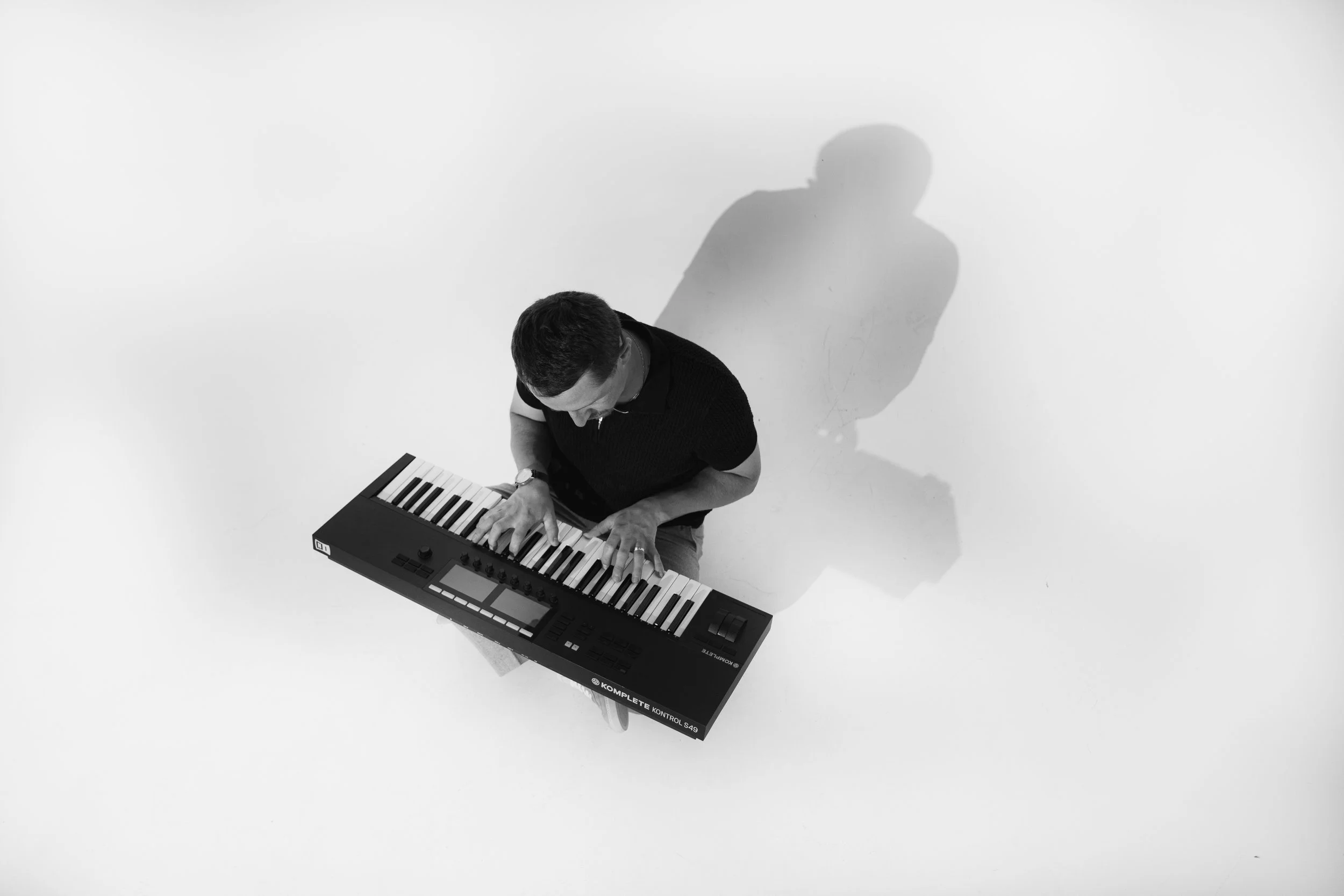 A man playing a keyboard seen from above, with his shadow cast on a plain white background.
