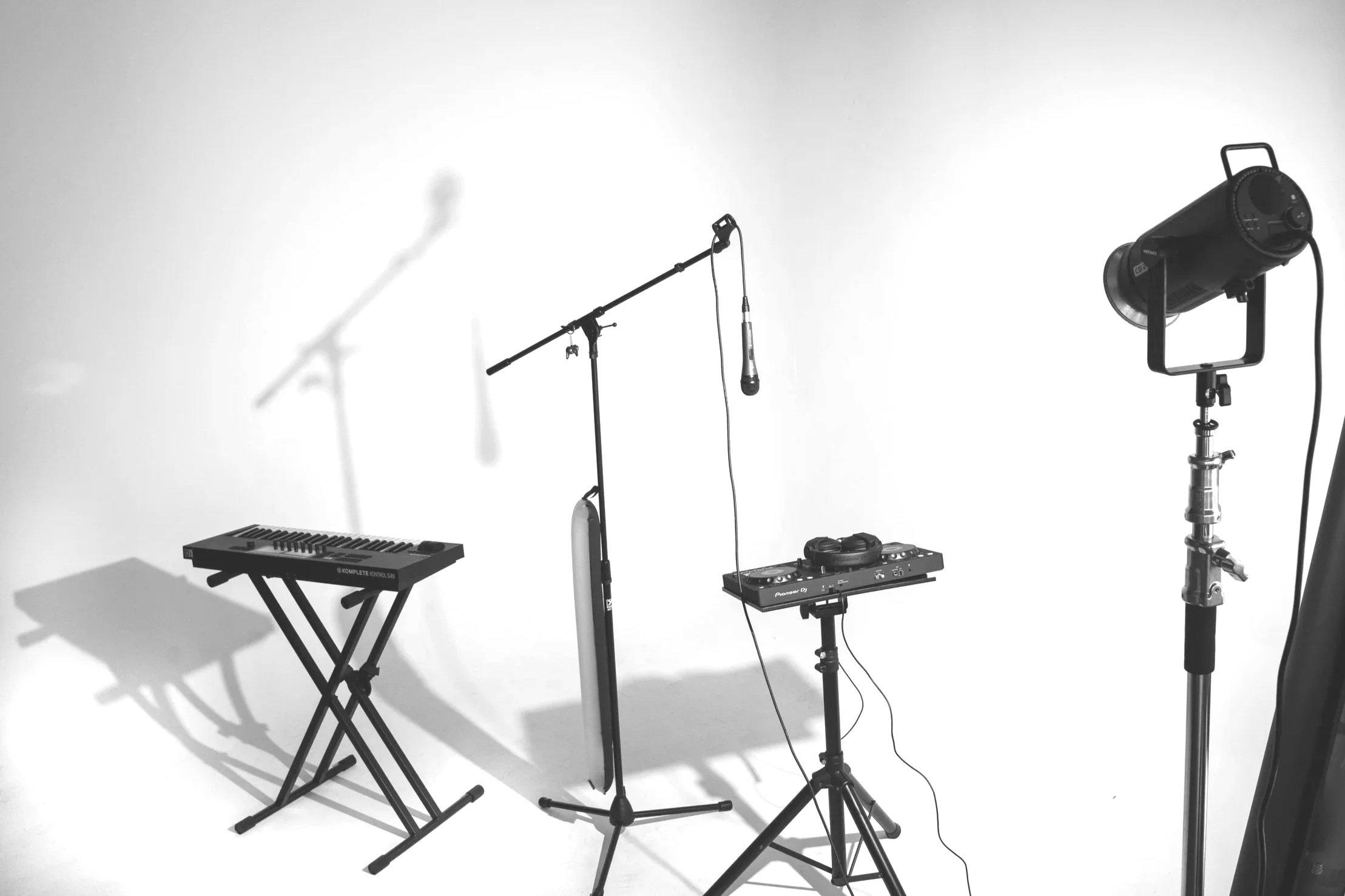 Music studio setup with a keyboard, microphone on stand, DJ controller, professional studio light, and shadows cast on a white wall.