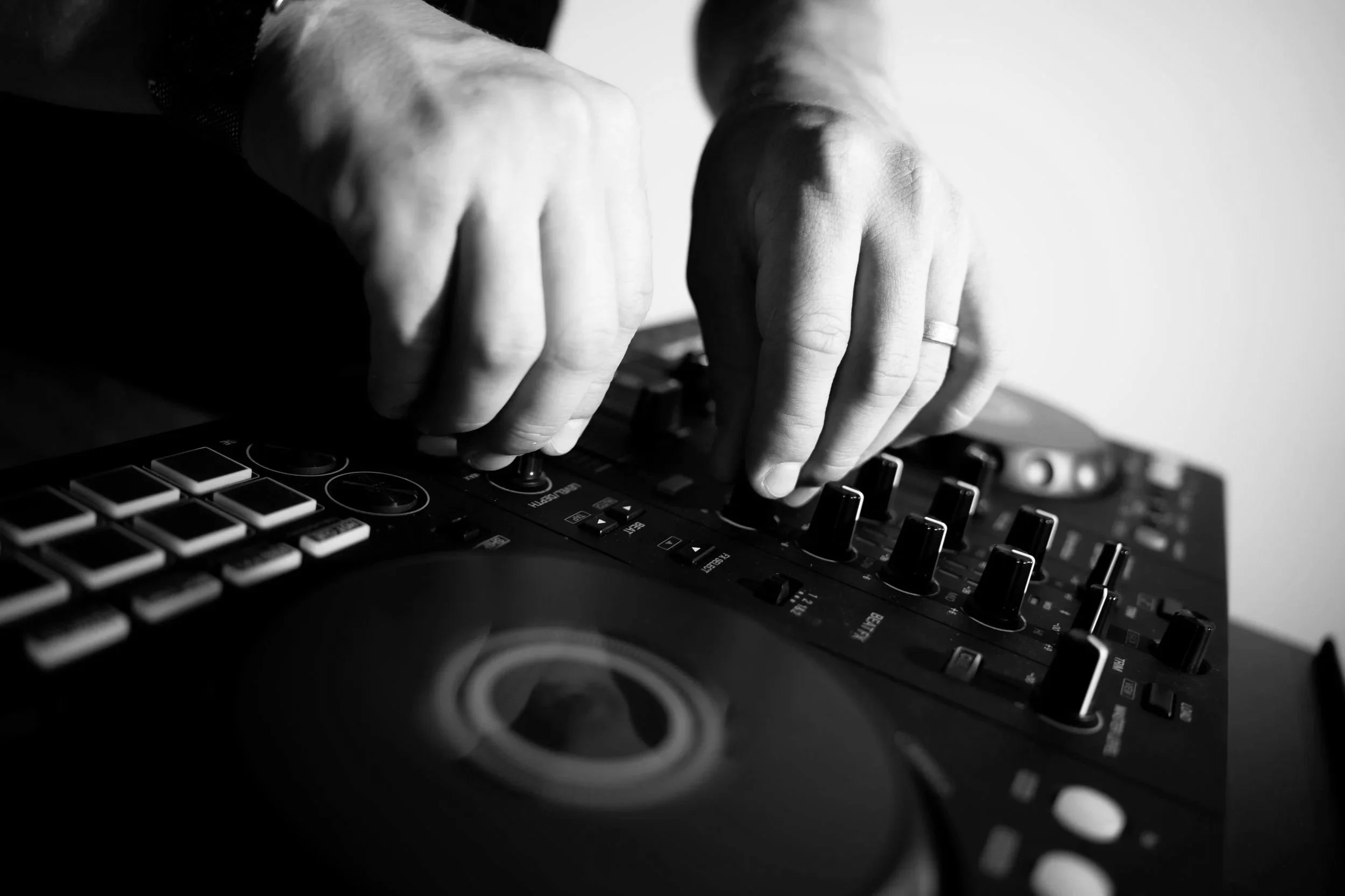 Close-up of hands manipulating DJ equipment with knobs and buttons in black and white