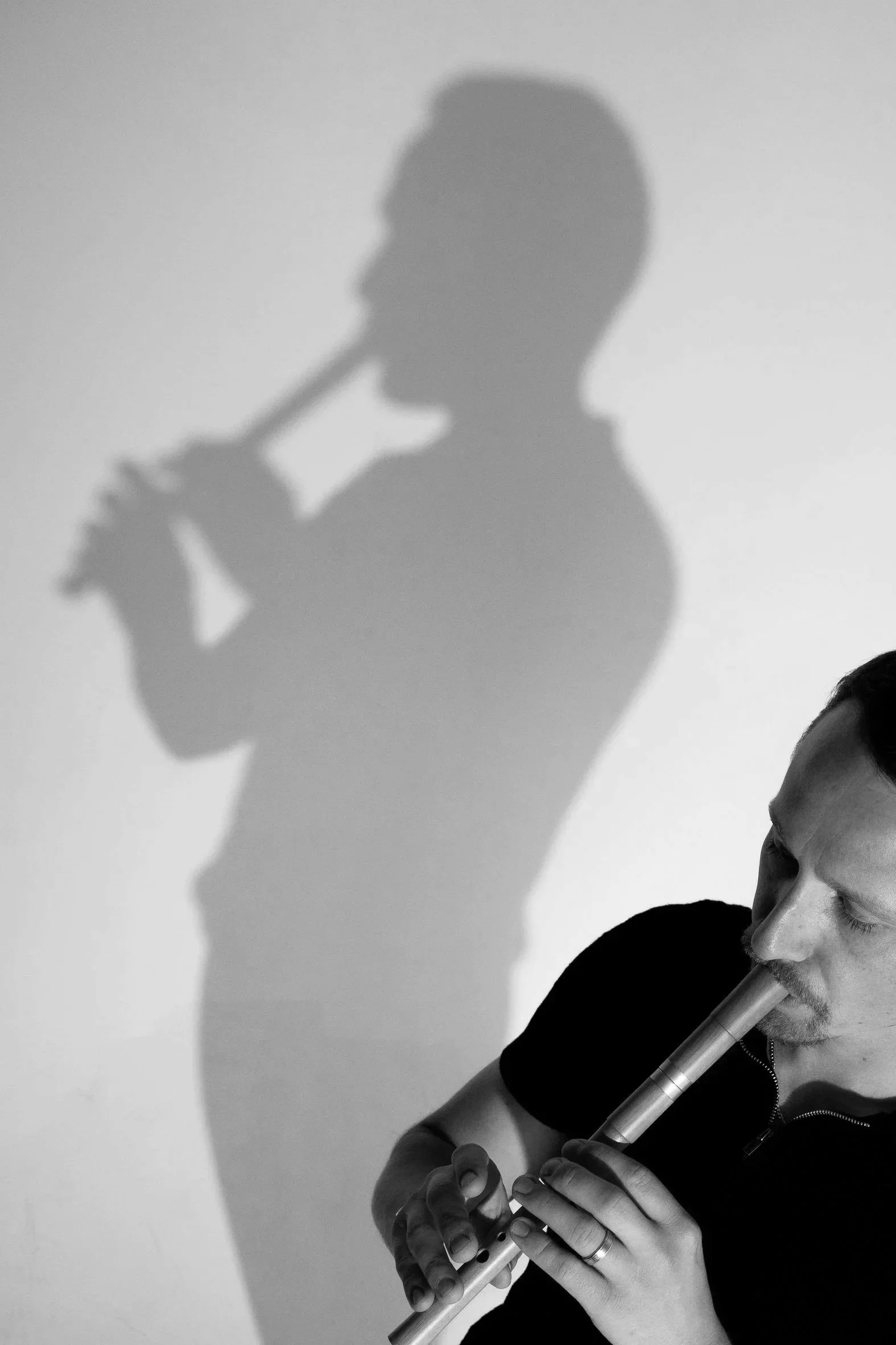 A man playing the flute with his eyes closed, casting a shadow on the wall that appears to be playing the flute too.