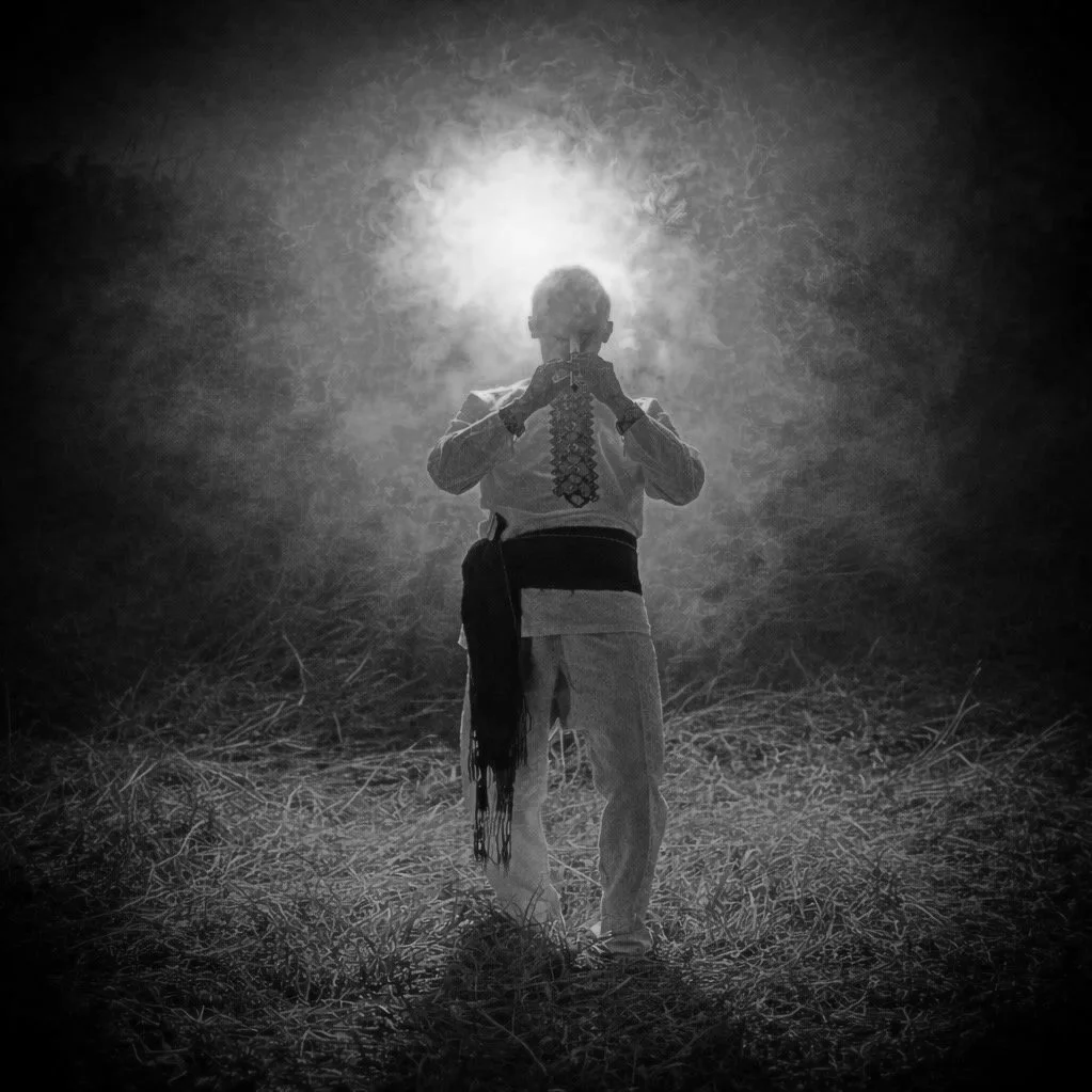 Person standing outdoors at night, facing the camera, with bright light behind their head creating a silhouette, in a grassy area.