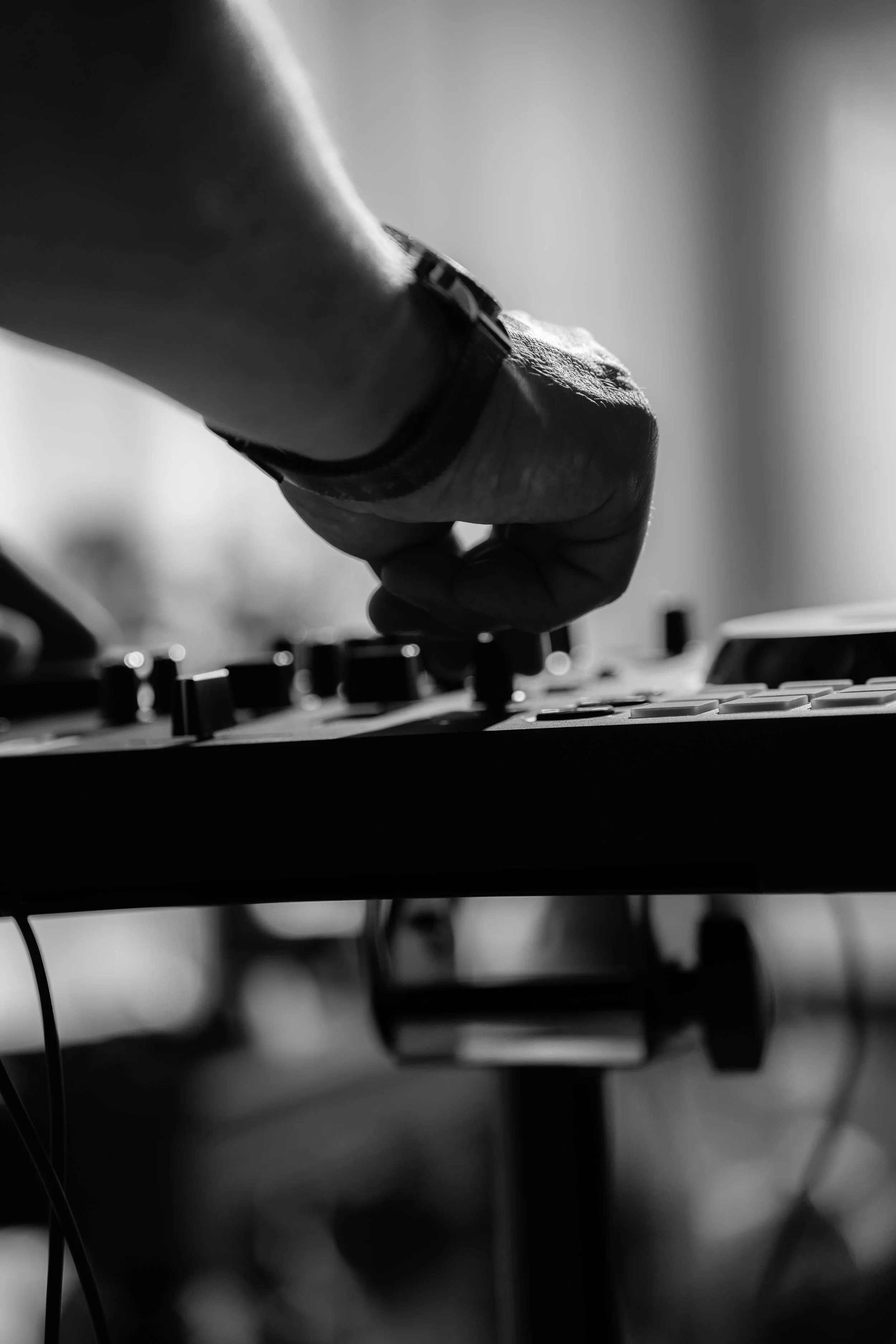 Close-up of a person manipulating a DJ mixer or turntable, with a focus on their hand and the control knobs, in black and white.