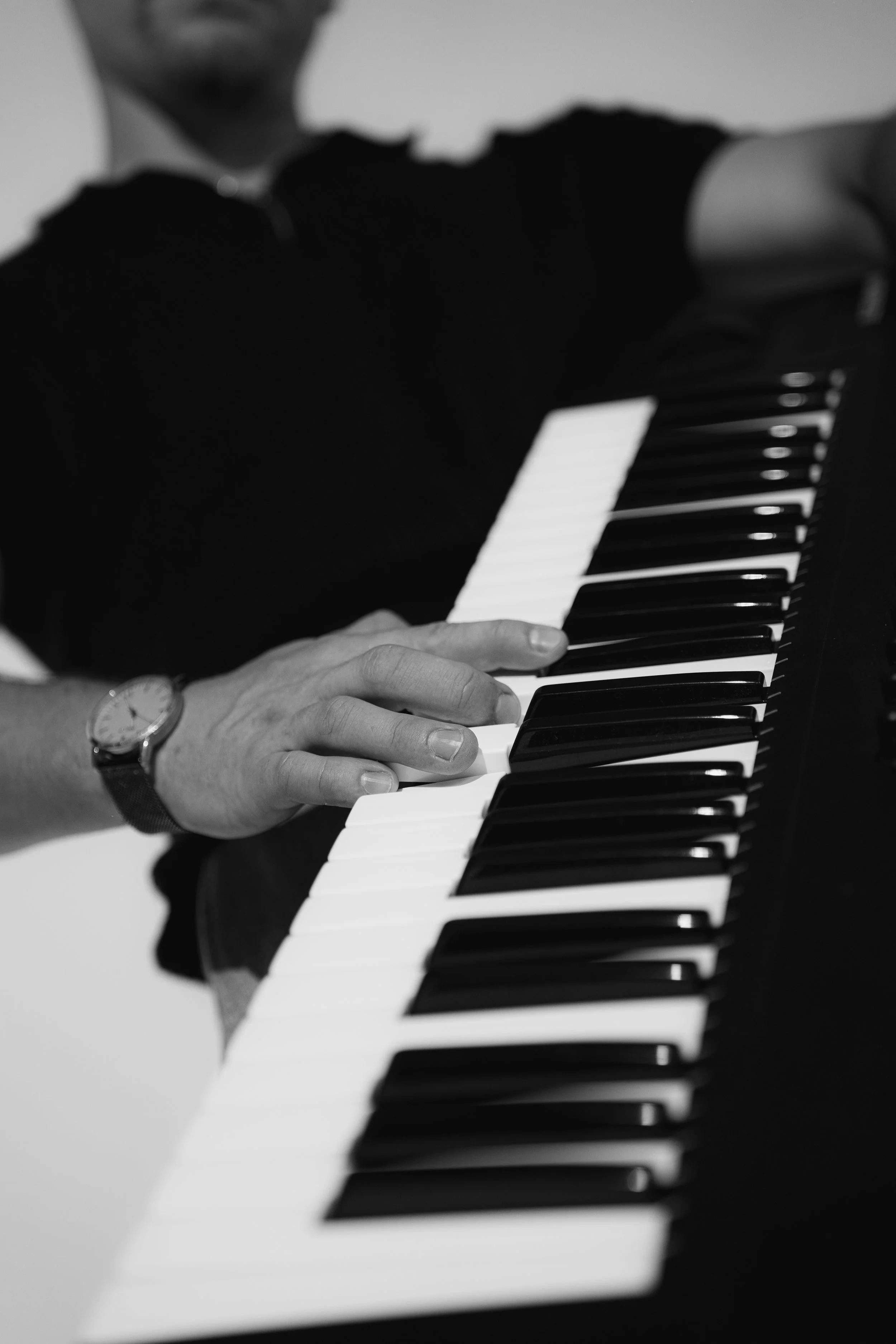 Black and white photo of a person playing the piano, with their hand on the keyboard and wearing a watch.