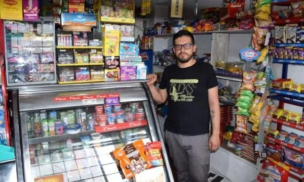 Hombre en tienda de abarrotes, con productos en refrigerador y estantes llenos de snacks y dulces.