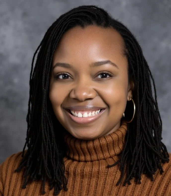 Portrait of a smiling young woman with dark braided hair, wearing a brown turtleneck sweater and hoop earrings, against a gray background.