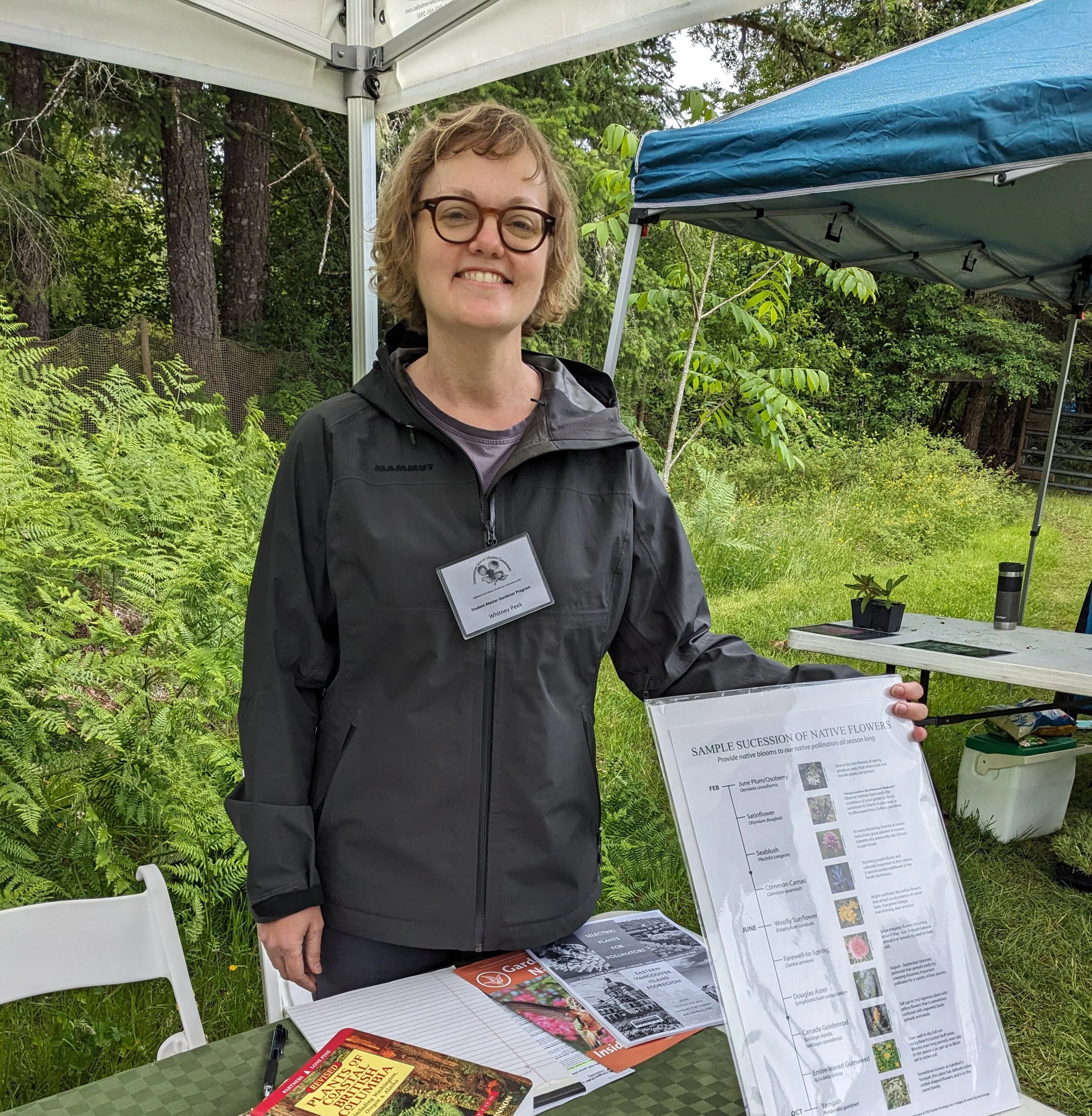 A person holding a poster at an outdoor event in front of a table with literature.